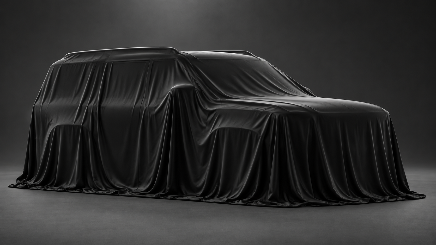 SUV draped in a black cover against a dark studio background
